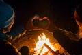 two people making heartshape with hands over a campfire at night