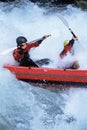 Two people paddling inflatable boat down rapids