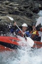 Two people paddling inflatable boat down rapids