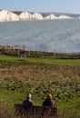 Two seated people admiring view of Seven Sisters chalk cliffs at Hope Gap, Seaford, E. Sussex on the south coast of England UK.