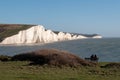 Two seated people admiring view of Seven Sisters chalk cliffs at Hope Gap, Seaford, E. Sussex on the south coast of England UK.