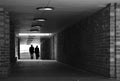 Two people silhouetted against a bright light walking through a tunnel with brick walls towards the camera monochrome Royalty Free Stock Photo