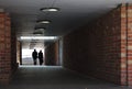 Two people silhouetted against a bright light walking through a tunnel with brick walls towards the camera Royalty Free Stock Photo