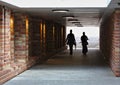 Two people silhouetted against a bright light walking through a tunnel with brick walls towards the camera Royalty Free Stock Photo