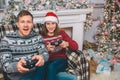 Two people sitting and playing games. Thay hold gamepads in hands. Young man and woman are excited. They push buttons