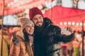 Two people students friends take selfie on cellphone girl make v-sign on outdoors x-mas christmas town event Royalty Free Stock Photo