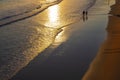 Two people walking along the shore of La Concha beach at sunrise