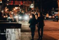 two people walking down the street at night, carrying hands and holding hands