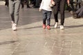 Two people wearing jeans and child girl wearing woolen clothing walking through the pedestrian walkway in summer vacation