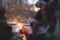 Two people warming hands with hot drinks by the bonfire. Spending nice time outdoors in chilly weather at a camping place - Royalty Free Stock Photo