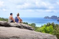 Two people young man and woman are sitting high on top of mountain, blue sea, sky with clouds and green trees beautiful view Royalty Free Stock Photo