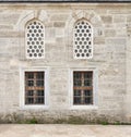 Two perforated arched stucco windows and two windows with bars on a weathered brick wall in Mihrimah Sultan Mosque