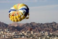 Two persons on a parachute over city and mountainous backdrop