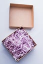Two-piece box is stuffed with purple shredded paper.