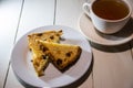 Two pieces of cake with raisins on a white plate and a white ceramic cup with tea on a white table from painted boards. Royalty Free Stock Photo