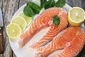 Two pieces of fresh salmon steak on a white plate with spinach and lemon, on  a gray wooden background. Omega 3 vitamin, healthy Royalty Free Stock Photo