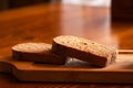 Two pieces of sliced black bread lie on a wooden board on a table in the sun, bread Royalty Free Stock Photo
