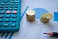 Two piles of coins over a paper full of charts and graphics, with a calculator and a pencil Royalty Free Stock Photo