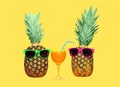 Two pineapple with sunglasses and glass fruit juice on yellow background