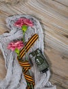 Two pink carnations, Saint George ribbon and military tank on a wooden surface