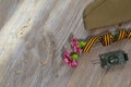 Two pink carnations, Saint George ribbon, tank, and military cap on a wooden surface