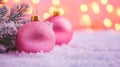 Two pink christmas ornaments sitting in the snow next to a pine tree Royalty Free Stock Photo
