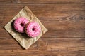 Two pink donuts on baking paper on wooden background, top view Royalty Free Stock Photo