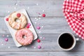 Two pink donuts decorated with smarties and sprinkles hearts and cup of coffee, wooden background