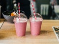 Two pink fruit milk cocktails smoothie in plastic cups with white-red spiral tubes for milkshakes stand on table Royalty Free Stock Photo