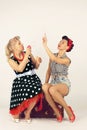 Two pinup girl friends sitting on a road suitcase and playing with soap bubbles on a white background Royalty Free Stock Photo