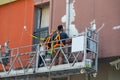 Two plasterers painters restoring the facade of the house staying in the building cradle Royalty Free Stock Photo