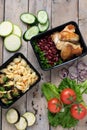 Two plastic containers with grilled chicken wings and raw vegetables on rustic background, vegetables salad