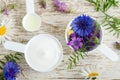 Two plastic scoops with various wild flowers and facial cream mask with herbal extracts. Ingredients of natural cosmetic. Royalty Free Stock Photo