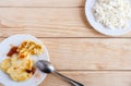 Two plates with curd and cheesecakes with plum jam and metal spoon are standing in opposite corners of wooden table. Royalty Free Stock Photo