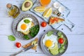 Two plates with fried eggs, toast, avocado, tomatoes, olive oil in a bottle, cutting board with lemon slices on a light Royalty Free Stock Photo