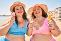 Two plus size overweight sisters twins women eating sweet ice cream at the beach on summer holidays Royalty Free Stock Photo