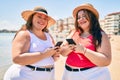 Two plus size overweight sisters twins women happy at the beach on summer holidays with smartphone