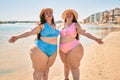 Two plus size overweight sisters twins women happy and proud of their bodies walking at the beach on summer holidays