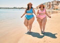 Two plus size overweight sisters twins women happy and proud of their bodies walking at the beach on summer holidays Royalty Free Stock Photo
