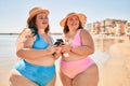 Two plus size overweight sisters twins women happy with smartphone at the beach on summer holidays Royalty Free Stock Photo