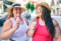 Two plus size overweight sisters twins women smiling eating an ice cream outdoors Royalty Free Stock Photo
