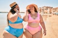 Two plus size overweight sisters twins women speaking on the phone at the beach on summer holidays