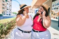 Two plus size overweight sisters twins women speaking on the phone outdoors on a sunny day