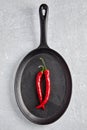 Two pods of red hot pepper in the shape of a female vulva in a black cast-iron frying pan on a light stone table