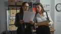 Two policewomen analyze documents in a cluttered office, suggesting an investigation in progress Royalty Free Stock Photo