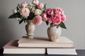 Two porcelain vases with delicate peon flower on stand of books on gray background.