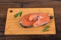 Two portioned salmon steaks with rosemary on a cutting board over a wooden background.