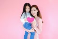 Two portrait beautiful cute asia child girl and woman on pink background with red heart sign holding in hand, valentine day in lov Royalty Free Stock Photo