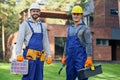 Rely on us. Two positive handsome young male engineers in hard hats smiling at camera, posing outdoors with toolbox and Royalty Free Stock Photo
