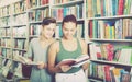 Two positive teenagers reading book together in shop Royalty Free Stock Photo